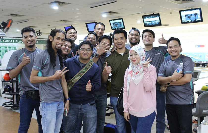 A group of 13 people smiling and holding peace signs in a bowling alley.