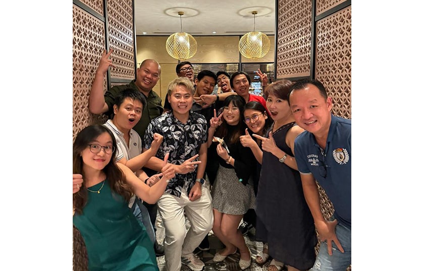 A group of 12 people smiling and overall happy holding their hands up at a restaurant.